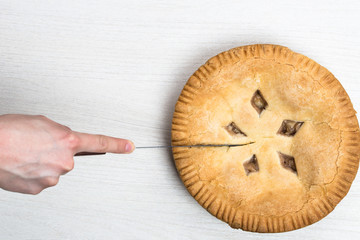 Apple pie cake lying on wooden white background with hand and knife
