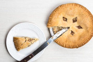 Apple pie cake lying on wooden white background with knife