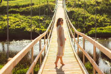 Beautiful girl standing on the center of the wooden bridge across the river