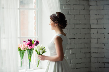 Beautiful bride with bouquet before wedding ceremony near window