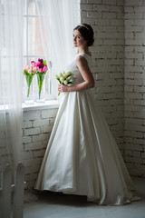 Beautiful bride with bouquet before wedding ceremony near window