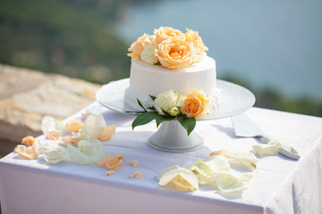 White wedding cake decorated with yellow and white roses outdoor