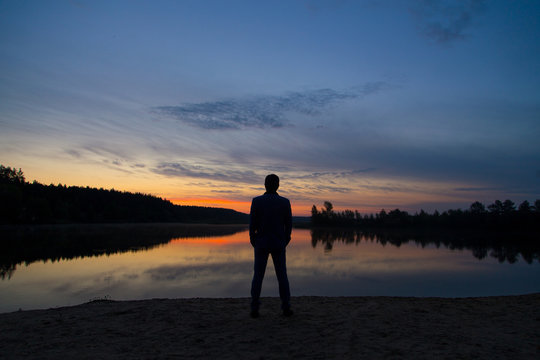 A man in a suit watches the sunset on the lake shore