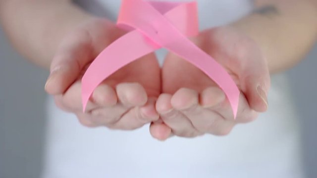 Womans hands holding out pink breast cancer awareness ribbon - breast cancer awareness concept