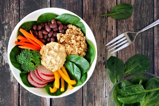 Healthy lunch bowl with quinoa, hummus and mixed vegetables, overhead scene on a rustic wood background