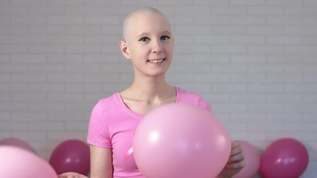 Happy breast cancer survivor woman smiling looking at the camera and playing with pink ballons - breast cancer awareness concept