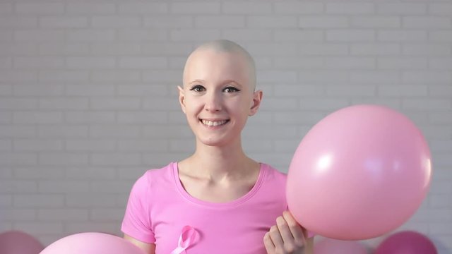 Happy breast cancer survivor woman appears out of pink ballons smiling and looking into the camera - breast cancer awareness concept