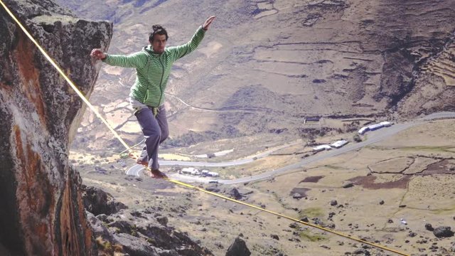 Slackliner balancing on tightrope between two rocks, Snowy mountains of the Huascaran park on the background, Peru. Slow motion