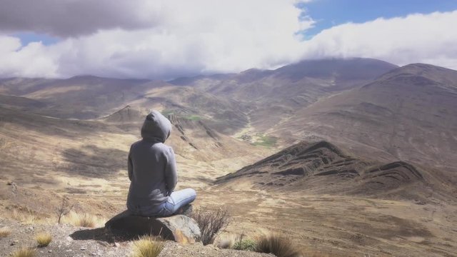 Back view of woman seated on the edge, admiring the nature of the Andean Mountains of Peru. 4k