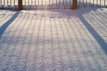 Metal decorative fence and the shadow of it falls flat lines on the snow.