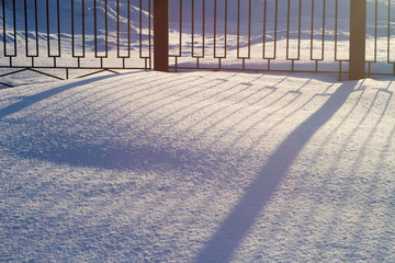 Snow is sparkles in sunny day and smooth shadow from beautiful fence.