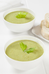 Two bowls of creamy celery soup with a garnish of celery leaves, served with crusty bread.