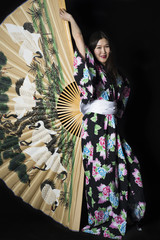 Japanese girl in traditional Japanese kimono with a large fan on a black background.