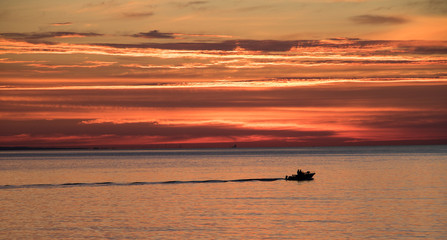 silhouette of boat underneath colorful sky at sunrise in summertime