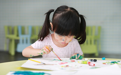 Child girl painting with paintbrush and water colors.