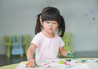 Child girl painting with paintbrush and water colors.