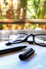 glasses and book on wooden table with soft-focus in the background. over light and film colors tone