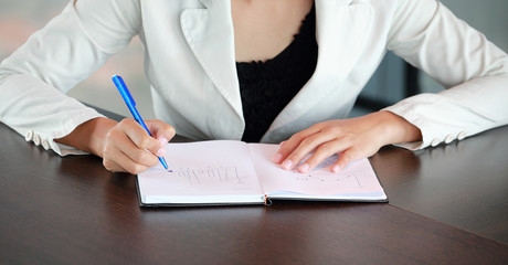 Close up young businesswoman sitting at the table on workplace in office and writing