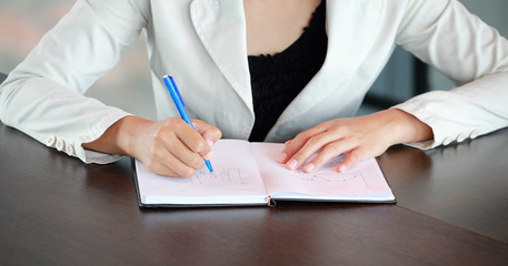 Close up young businesswoman sitting at the table on workplace in office and writing