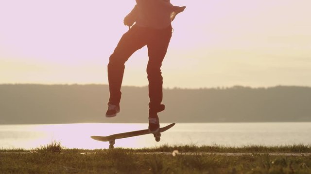 SLOW MOTION, CLOSE UP: Silhouetted skateboarder skateboarding and jumping 360 flip trick on promenade along the ocean at golden light sunset. Skateboarder riding skateboard at sunrise at seaside