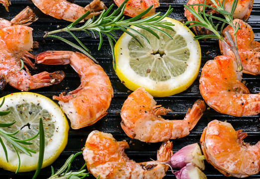 Shrimps roasted on grill pan with lemon slices and rosemary.