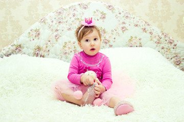 Charming little girl is sitting on the bed with a toy and is having fun playing