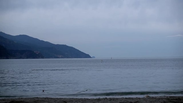 Morning swim in the Mediterranean sea, man doing the crawl in a gloomy, grey, and sad atmosphere, cold weather, next to the beach in Cinque Terre, Italy. 4K