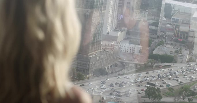 Beautiful young blonde woman looks down past her reflection in window at traffic on the 110 freeway in Downtown Los Angeles. Over the shoulder shot, recorded hand-held in slow motion at 60fps