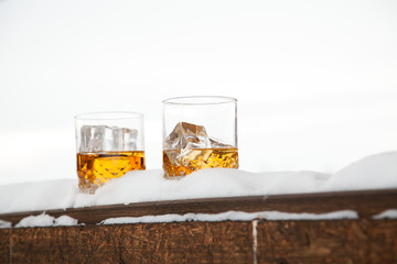 Two whiskey glasses in the snow on a winter background.