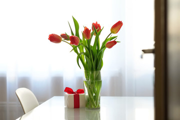 Bouquet of red tulips in a glass vase on a glass table, gift