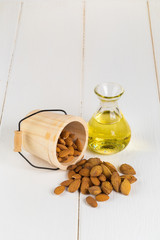 Bottle of almond oil and almonds on white wooden background.