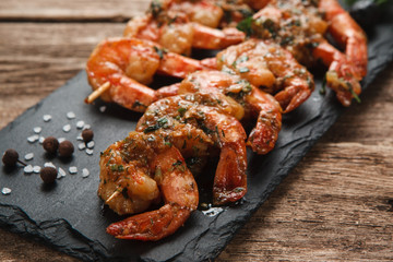 Japanese seafood. Fried spicy shrimps with herbs on wooden skewers served on black slate, close up view.
