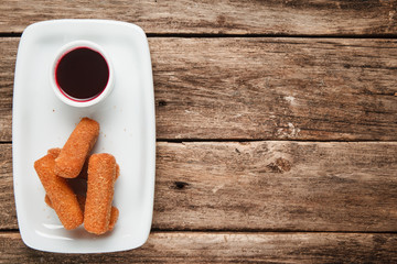 American fast food. Fried chicken nuggets on white plate served with sweet chili sauce, flat lay. Wooden background with copy space.
