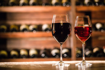 Close-up shot of two wine glasses filled with red wine. COmposition on a wooden table.