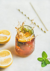 Summer cold Iced tea with fresh bergamot, mint and lemon in glass jar with splashes on light table background. Food in motion concept