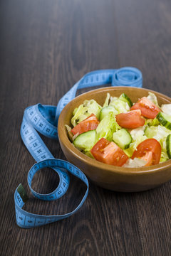 Salad in wooden bowl and measuring tape on a table close-up.