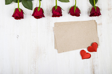 Red roses and paper for congratulations on a wooden background.