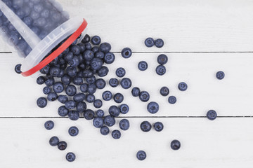 Blueberries falling out of plastic bucket on white wood