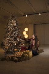 Woman sitting under Christmas tree with gift parcels