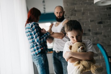 Sad child hugging his teddy bear during parents quarrel. - obrazy, fototapety, plakaty