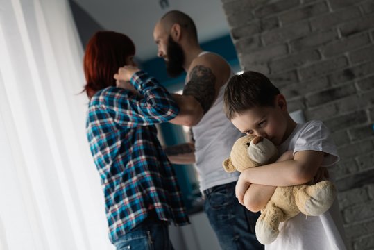 Sad child hugging his teddy bear during parents quarrel.