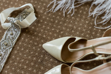Wedding decoration details. Еlegant bridal shoes on a brown carpet, ostrich white feather and white ribbon with bright stones.