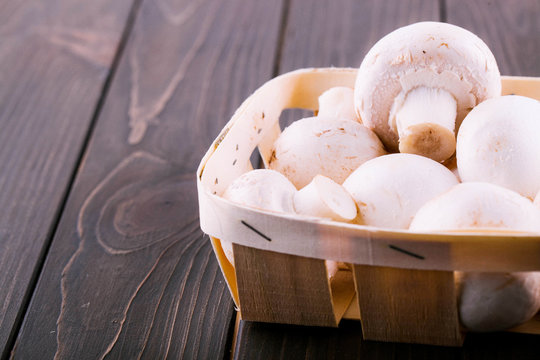 White mushrooms lie on basket on dark wooden table