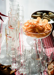 Potato chips served in glass bowl stand among empty glasses
