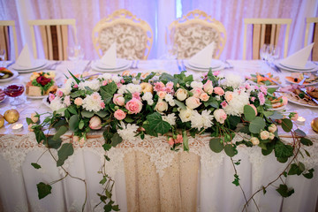 Garland made of pink roses and green leaves lies on white dinner table