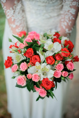 Bouquet of red roses and lilies held by bride in dress with laces