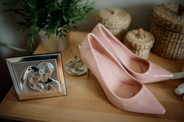 Pink wedding shoes stand behind steel icon on wooden table