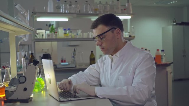 doctor at working place forensics science or chemist engineer working with laptop in laboratory. Adult man wearing in lab coat typing on computer.