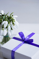 Beautiful white snowdrops with gift box on white wooden background