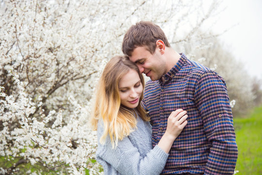 Young romantic couple standing in front of wonderful blooming trees in spring garden